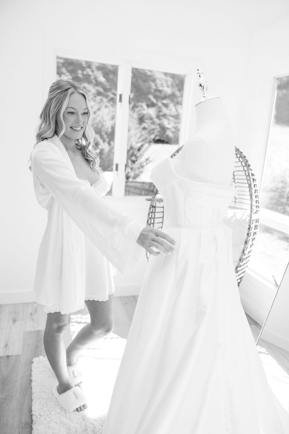 Black-and-white photo of a bride in a robe beside her wedding gown
