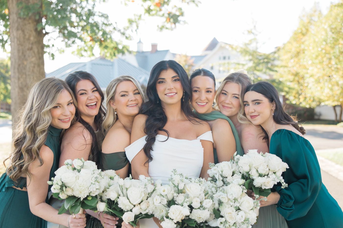 Bride with bridesmaids in emerald green dresses holding white rose bouquets
